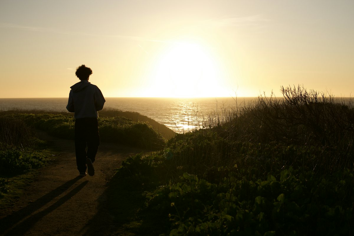 A person walking along a path towards the sun.