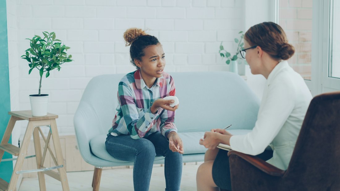 A practitioner talking with a young person seated on a couch.