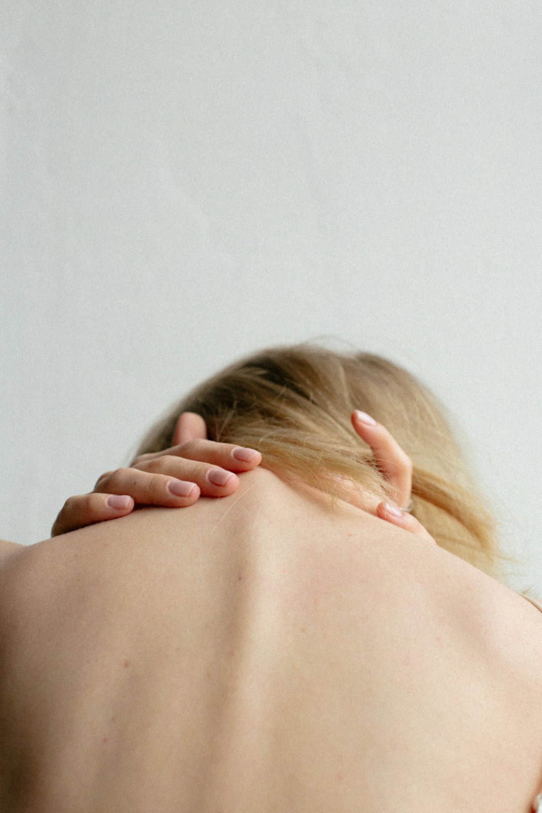 A person reaching a hand to the back of their neck and shoulder.