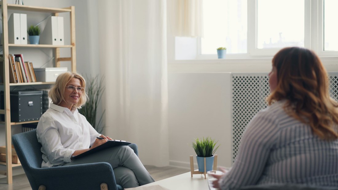 A practitioner and a client talking in armchairs in a bright, quiet room.