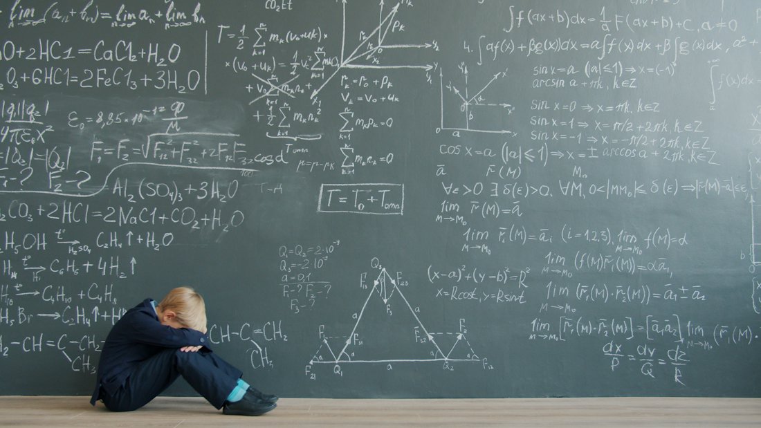 A student sitting beside a blackboard covered in equations.